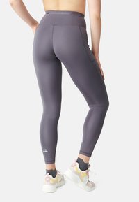 Hoge taille, aansluitende legging in donkergrijze stof met stretch. Bevat subtiele stiksels en een klein logo bij de enkel. Gecombineerd met witte en pastel sneakers.