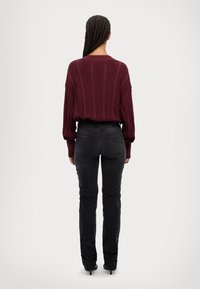 Jersey burdeos de punto trenzado con mangas oversized combinado con unos jeans negros de talle alto, mostrando textura y una silueta ajustada por la parte de atrás.