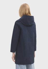 Tmavě modrá bunda s kapucí vyrobená z lehkého materiálu. Má dlouhé rukávy a rovný střih, navržena pro casual nošení.