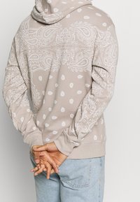 Felpa beige con motivi a paisley bianchi e punti, maniche lunghe, tasca a marsupio e polsini a costine sui polsi e sull'orlo.