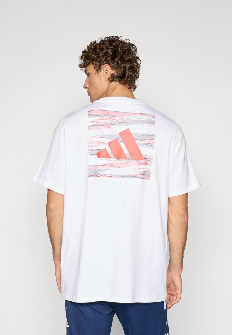 Hvid bomuld t-shirt med et stort pink og gråt abstrakt Adidas-logo på ryggen. Kortærmet og en afslappet pasform.