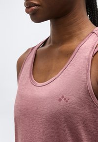 Primer plano de una persona que lleva una camiseta deportiva sin mangas de color rosa polvo con un pequeño logo en el pecho.