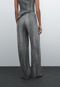 Szare lniane spodnie o szerokich nogawkach z fakturowanym wykończeniem, wysoki stan i delikatne fałdy. Posiadają luźny krój i czysty, minimalistyczny design.