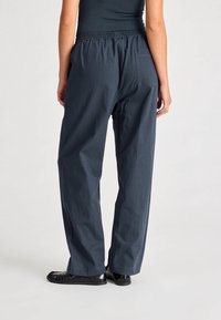 Pantaloni blu navy, dalla vestibilità ampia con vita elastica, dotati di una tasca posterior e una texture liscia. Abbinati a scarpe nere.