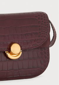 Borsa in pelle stampata coccodrillo color bordeaux con una chiusura circolare dorata e una tracolla corta, caratterizzata da una consistenza liscia e bordi arrotondati.