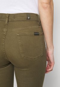 Pantalones de mezclilla verde oliva con un diseño ajustado, que cuentan con una etiqueta en la cinturilla y dos bolsillos traseros con detalles de costura.