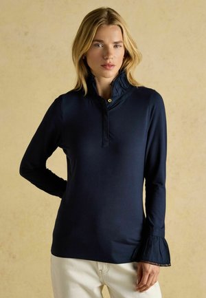 Meriinisinine pika varrukaga särk kõrge kraega ja volangidega, millel on nööpidega sulgur ja lehvitavad varrukapikendused. Sile, elastne kangas.