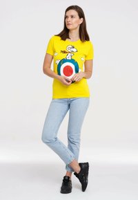 Yellow T-shirt with a graphic of Snoopy on a target design. Light blue jeans and black sneakers complete the outfit. Simple design, casual fit.