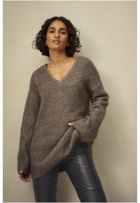 Bruine, oversized trui met een V-hals en lange mouwen, gemaakt van zachte, gestructureerde stof; gecombineerd met strakke zwarte leren broek.