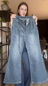 Ανοιχτό μπλε τζιν παντελόνι με φαρδιά γραμμή, διαθέτοντας μπροστινό φερμουάρ και κλείσιμο με ζώνη. Το ύφασμα έχει ξεθωριασμένη όψη με ελαφριές τσακίσεις.