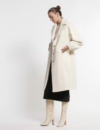 Lång, krämfärgad kappa med bred krage, knappstängning och strukturerade ärmar. Matchas med en svart kjol och krämfärgade knähöga stövlar.