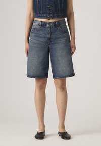 Shorts en denim bleu moyen, longueur mi-cuisse avec une coupe droite, dotés d'une fermeture à bouton et fermeture éclair, ainsi que d'un design classique à cinq poches.