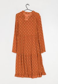 Rostorange långärmad klänning med vita prickar, flerlagersdesign, volangkjol och knäppta manschetter. Hänger på en svart krok.