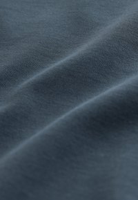 Textile in dark blue, showing a smooth texture and fine knit pattern, with subtle ripples indicating softness and flexibility.