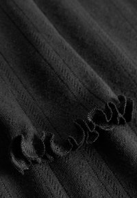 Čierna tkanina s vertikálnou ryhou textúrou, s riaseným okrajom. Materiál pôsobí mäkko s jemným leskom. Celkový hladký povrch.