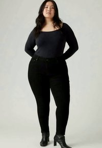 Črne visokotlačne kavbojke s slim fit krojem in diskretno šivanko, v kombinaciji z oprijeto dolgimi rokavi mornarsko modre majice in gležnjarji.