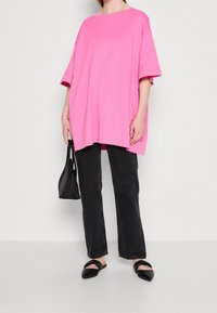 Camiseta de algodón rosa de gran tamaño con mangas cortas, combinada con jeans negros de pierna recta y zapatos planos negros. Accesorios con un bolso negro.