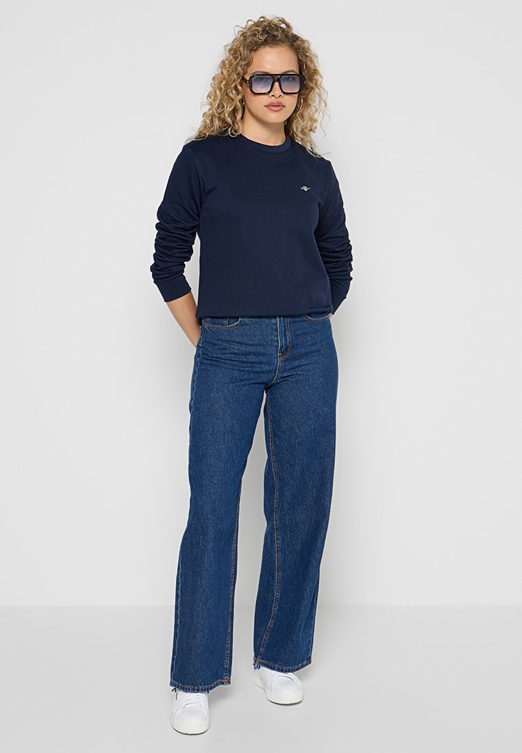 Marineblauer Sweatshirt aus Baumwolle mit Rundhalsausschnitt. Kombiniert mit hoch sitzenden, weit geschnittenen blauen Jeans und weißen Sneakers.