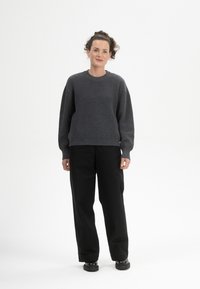 Grau gestrickter Pullover mit runden Ausschnitt und gerippter Textur, kombiniert mit schwarzen weit geschnittenen Hosen und klobigen schwarzen Schuhen.