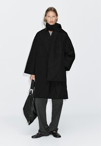Black lightweight coat with a high neck, long sleeves, and a matching scarf. Paired with dark gray trousers and a black leather bag.