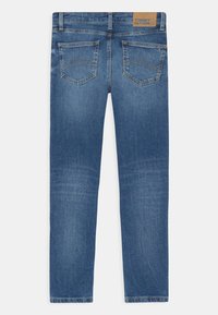 Vaqueros de mezclilla azul con corte recto, cinco bolsillos y un parche de cuero marrón con el logo de la marca en la cinturilla. Textura con un desgaste uniforme.