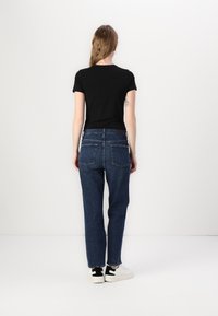Top negro de manga corta combinado con jeans oscuros de cintura alta, con un corte relajado, piernas rectas y dos bolsillos traseros. Zapatillas deportivas blancas con un acento negro.
