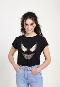 Sort bomulds T-shirt med et grafisk design af et hvidt og rødt sultent ansigt med skarpe tænder. Båret med lyseblå højtaljede jeans.