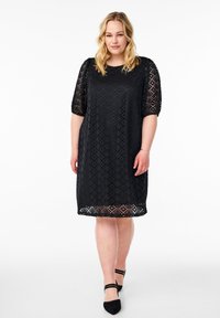 Vestido de encaje negro con un corte holgado, mangas cortas abullonadas, escote redondo y un dobladillo a la altura de la rodilla con un patrón de calado.