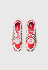 Scarpe da ginnastica in rete rossa con accenti bianchi, caratterizzate da un design elegante, strisce nere e una suola texturizzata. Lacci bianchi.