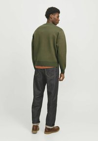 Suéter de punto verde oscuro con dobladillo acanalado, combinado con jeans de color claro. El modelo está de espaldas, mostrando un ajuste relajado.