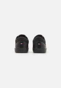 Czarne sneakersy z teksturowaną cholewką, średnią podeszwą i tylnym uchwytem z małym logo; minimalistyczny design z krzywymi przeszyciami.