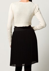 Beskuren krämfärgad tröja med ribbat avslut i kombination med svart plisserad kjol. Tröjan har långa ärmar och en mjuk textur.