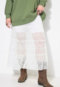 Bílá krajková maxi sukně s patrovým designem, poloprůhledná tkanina, nošena na hnědých kožených kovbojských botách, zkombinována s olivově zelenou mikinou.