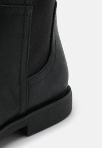 Svart läderankelboot med en strukturerad ovandel, platt gummisula och subtila stickningsdetaljer. Har en elegant, rundad design.