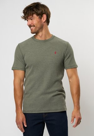 Short-sleeved green knit t-shirt with a round neckline and red logo detail on the left chest. Fabric appears textured and breathable.