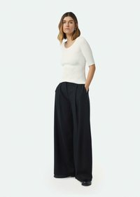 Witte geribbelde top met korte mouwen, gecombineerd met hoge taille zwarte wijde pantalon, voorzien van zijzakken en een soepele, gestructureerde stof.