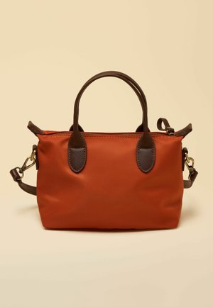 Rechteckige Handtasche in Rostfarbe mit dunkelbraunen Griffen und abnehmbarem Schulterriemen, vor einem beigen Hintergrund präsentiert.