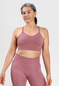 Lichtroze sportbeha en high-waisted legging in een gladde, rekbare stof. Heeft dunne banden en een aansluitend ontwerp voor comfort en ondersteuning.