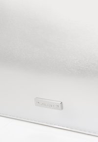 Pochette argentata metallica con una superficie liscia, dotata di una piccola placca con logo inciso e design minimalista.