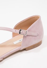 Chaussure plate en daim rose clair avec une fine bride à la cheville et une boucle argentée, avec un talon fermé et une semelle couleur beige.