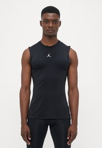 Zwart mouwloos sporttop gemaakt van gladde, rekbare stof. Bevat een wit Jumpman-logo op de borst. Vormgeving die aansluitende is.