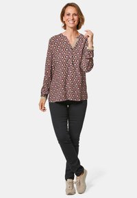 Langärmlige Bluse mit einem gemusterten Design in Rot, Weiß und Dunkelrot, kombiniert mit schwarzen Slim-Fit-Hosen und beigen Sneakern.