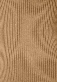 Tissu en maille côtelée de couleur beige chaud, présentant des rayures verticales qui créent un aspect texturé. Texture douce et design extensible.