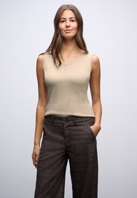 Top sin mangas de color beige con escote en V y pequeños detalles de botones, combinado con pantalones de cuadros marrón oscuro de corte relajado y con bolsillos laterales.