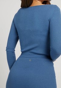 Vestito a maglia blue a coste con maniche lunghe e silhouette aderente. Presenta un piccolo accento di logo silver in vita. Tessuto morbido e design aderente.