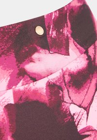 Tkani pas z različnimi odtenki roza in bordo barve z vzorcem cvetja. Vsebuje majhen bronast okrasni gumb.