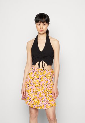 Top cropped preto com alças, com frente franzida e laço ajustável, combinado com uma saia rodada floral rosa com detalhes amarelos e pretos.