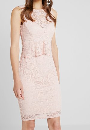Bezrękawnikowa, jasnoróżowa koronkowa sukienka z kwiatowym wzorem, z detalem w talii typu peplum i długością do kolan, noszona przez stojącą kobietę.