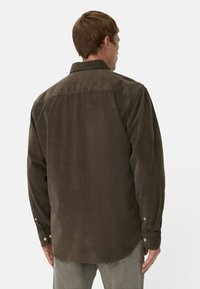 Brązowa koszula z korduroy z wyłamiem typu pointed, mankietami na guziki oraz zaokrąglonym dołem. Tkanina ma miękką teksturę i lekko postarzany wygląd.