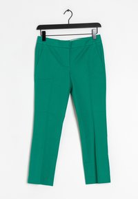 Pantalons taper verts avec une texture lisse, dotés de deux poches latérales et d'une fermeture éclair. Accrochés à un cintre en plastique noir.